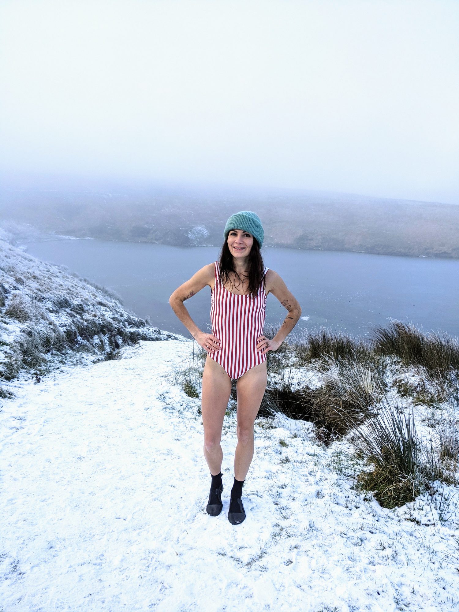 Woman on a snow covered beach wearing a swimming costume with a warm hat